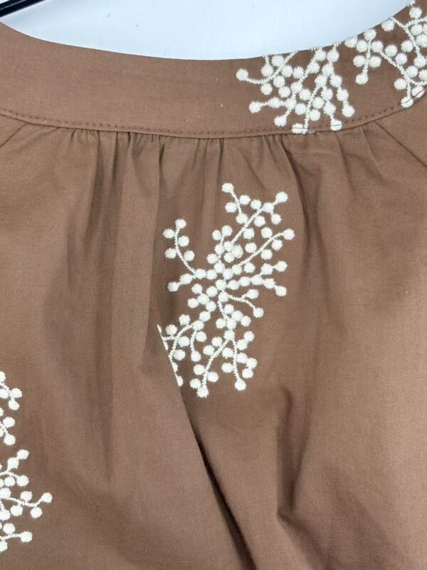 Close-up of a brown skirt featuring intricate white embroidery floral patterns at the waist and hem, showcasing stylish and detailed design.