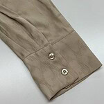 Close-up of a beige satin shirt cuff with two shiny silver buttons, showcasing luxurious fabric and fine craftsmanship.