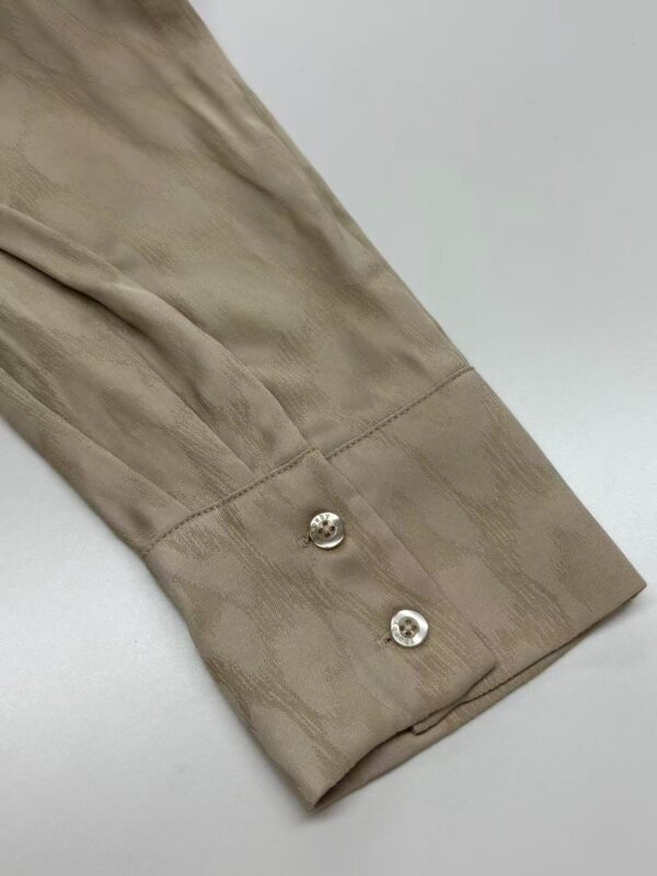 Close-up of a beige satin shirt cuff with two shiny silver buttons, showcasing luxurious fabric and fine craftsmanship.