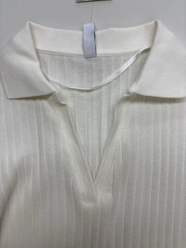 Close-up of a white ribbed polo shirt with a V-neck collar, displayed on a hanger, showcasing its soft fabric and classic design.