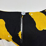 Close-up of a black dress with bold yellow abstract patterns and a small white button at the neckline, showcasing stylish and modern design.