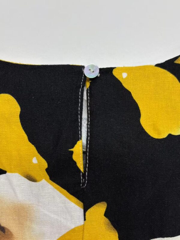 Close-up of a black dress with bold yellow abstract patterns and a small white button at the neckline, showcasing stylish and modern design.