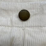 Close-up of a black Bonobo button on cream-colored textured fabric with a zipper detail, showcasing high-quality clothing material.