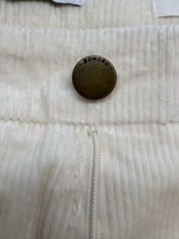 Close-up of a black Bonobo button on cream-colored textured fabric with a zipper detail, showcasing high-quality clothing material.