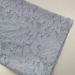 Close-up of white lace fabric with intricate floral patterns, ideal for fashion and wedding dress design.