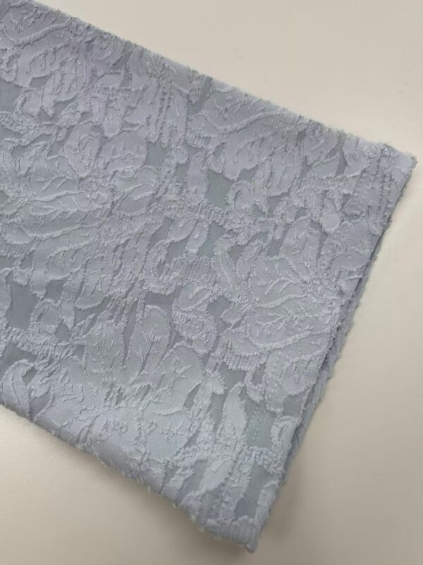 Close-up of white lace fabric with intricate floral patterns, ideal for fashion and wedding dress design.