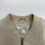 Close-up of a beige zip-up casual jacket for women, featuring a round neckline and a small brand label inside. Perfect for everyday wear and stylish comfort.