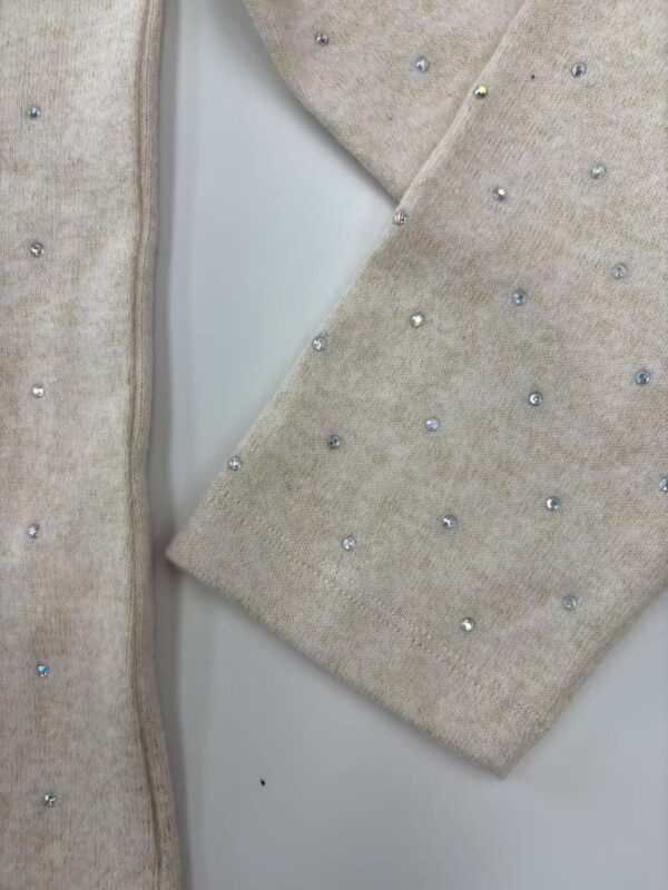 Close-up of beige knit fabric with small, colorful beads for luxury fashion design.