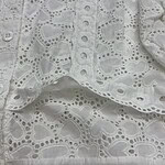 Close-up of white eyelet lace fabric with intricate heart and floral patterns, showcasing detailed embroidery and cutwork for fashion and textile design.