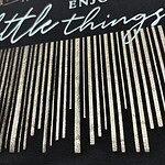 Close-up of fabric with an inspirational quote 'Enjoy the little things' in elegant script, featuring a striped pattern background.