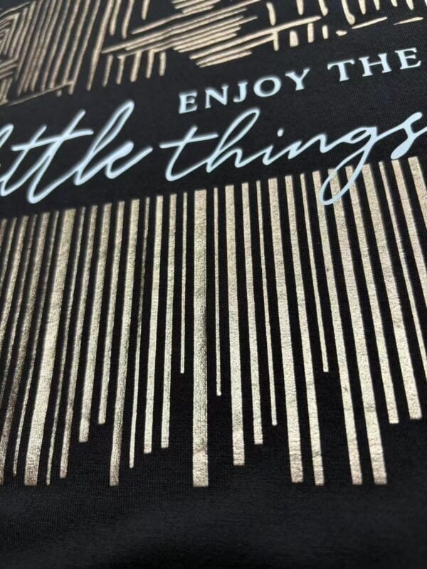 Close-up of fabric with an inspirational quote 'Enjoy the little things' in elegant script, featuring a striped pattern background.
