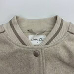 Close-up of a beige cotton cardigan with a round neckline, button closure, and striped ribbed collar, perfect for casual or semi-formal wear.