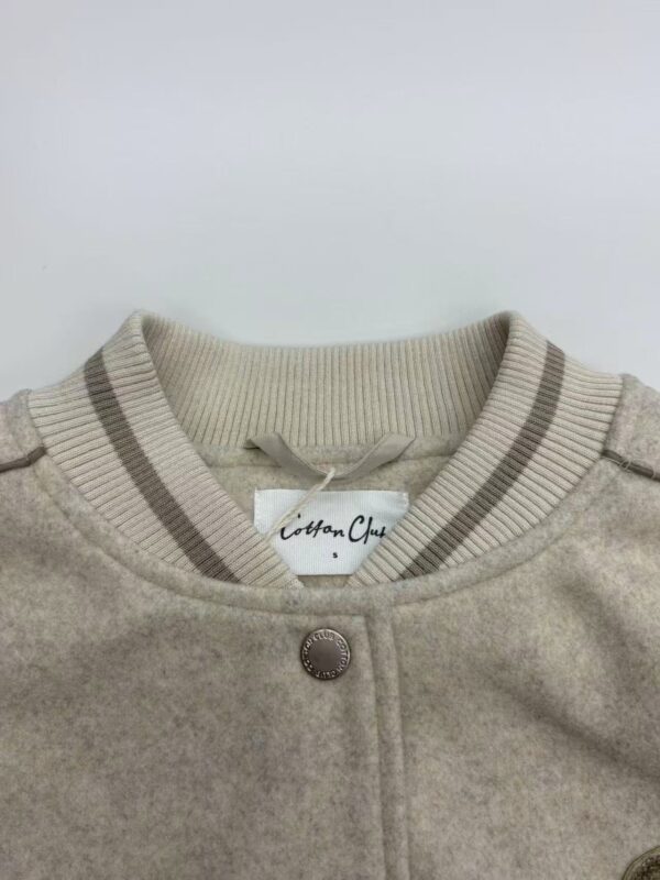 Close-up of a beige cotton cardigan with a round neckline, button closure, and striped ribbed collar, perfect for casual or semi-formal wear.