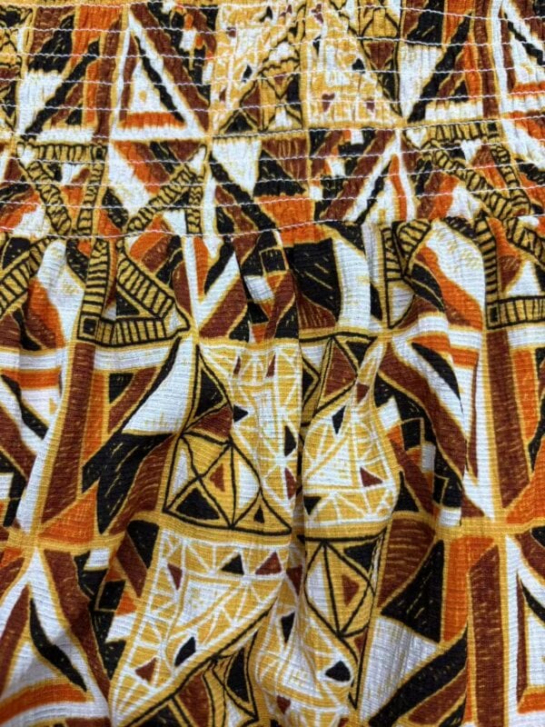 Close-up of vibrant African tribal pattern fabric with geometric shapes in orange, black, white, and yellow colors, showcasing traditional textile design.