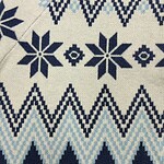 Close-up of Nordic-inspired knit fabric with geometric snowflake and zigzag patterns in navy blue and light blue on cream background.