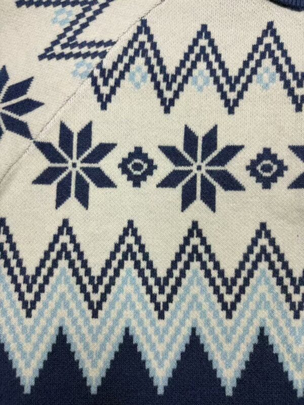 Close-up of Nordic-inspired knit fabric with geometric snowflake and zigzag patterns in navy blue and light blue on cream background.