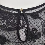 Close-up of black lace fabric with a decorative neckline featuring a small jewel and a black ribbon tie, showcasing intricate lace patterns and fine craftsmanship.