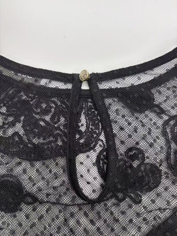 Close-up of black lace fabric with a decorative neckline featuring a small jewel and a black ribbon tie, showcasing intricate lace patterns and fine craftsmanship.