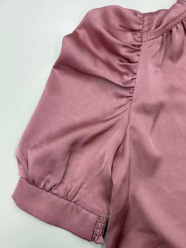 Close-up of a pink satin blouse with ruched sleeve detail and cuff, showcasing luxurious fabric and stylish design for women's fashion.