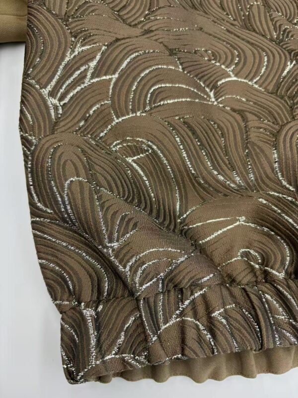 Close-up of a brown dress with intricate sequin embroidery and textured fabric, showcasing luxurious design and craftsmanship.