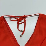 Close-up of a vibrant red V-neck dress featuring a tie detail at the neckline, perfect for stylish summer or evening wear.