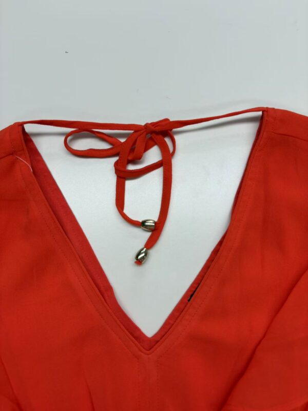 Close-up of a vibrant red V-neck dress featuring a tie detail at the neckline, perfect for stylish summer or evening wear.