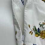 Close-up of a white dress featuring a floral pattern with yellow and green accents, and a zipper detail.