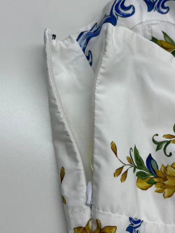Close-up of a white dress featuring a floral pattern with yellow and green accents, and a zipper detail.