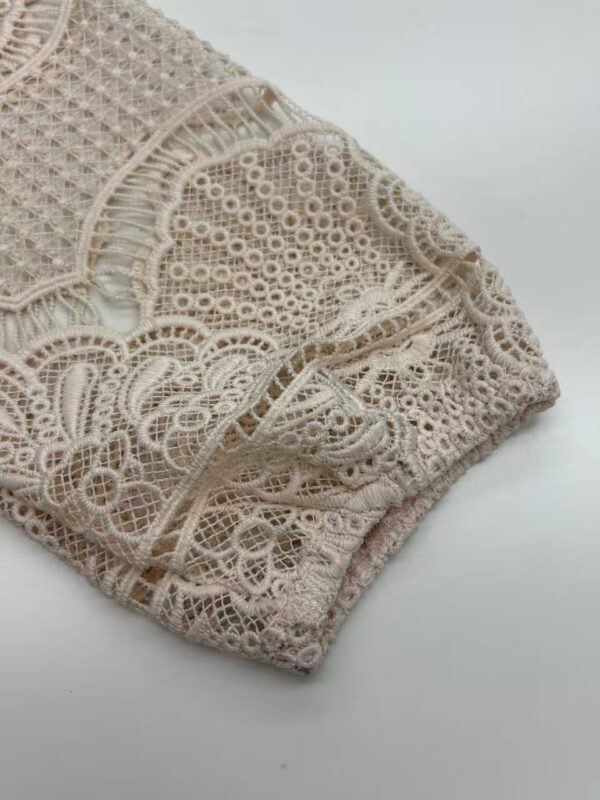 Close-up of intricate beige lace fabric with detailed embroidery and openwork patterns, ideal for fashion and textile projects.