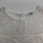 Close-up of a white lace blouse with intricate floral patterns and a round neckline, perfect for stylish summer or spring outfits.
