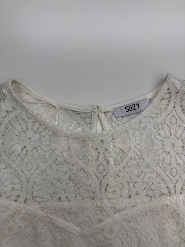 Close-up of a white lace blouse with intricate floral patterns and a round neckline, perfect for stylish summer or spring outfits.