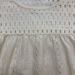 Close-up of a cream-colored eyelet dress with intricate cut-out patterns and a gathered waist, perfect for summer or casual occasions.
