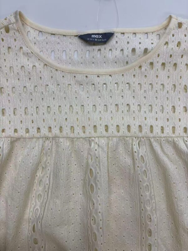 Close-up of a cream-colored eyelet dress with intricate cut-out patterns and a gathered waist, perfect for summer or casual occasions.
