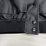 Close-up of black leather jacket with snap buttons and elastic waistband, showcasing stylish and durable fashion design.
