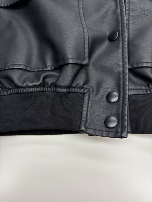 Close-up of black leather jacket with snap buttons and elastic waistband, showcasing stylish and durable fashion design.