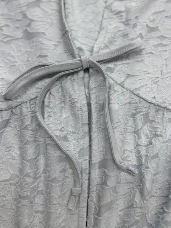 Close-up of a white lace dress featuring intricate floral patterns and a satin bow tie at the waist, perfect for formal occasions.