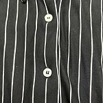 Close-up of a black shirt with white vertical pinstripes and white buttons, showcasing a modern and elegant design.