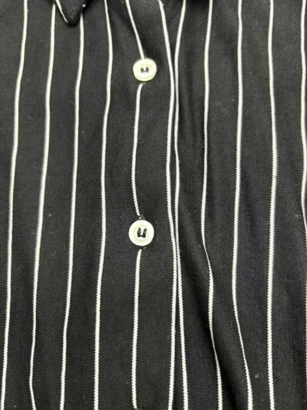 Close-up of a black shirt with white vertical pinstripes and white buttons, showcasing a modern and elegant design.