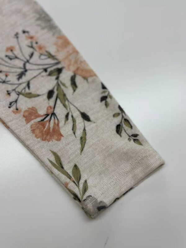 Close-up of a fabric sleeve with a delicate floral pattern featuring peach, green, and black accents on a light background.
