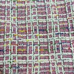 Close-up of vibrant pink, yellow, blue, and white tweed fabric with a textured woven pattern, ideal for fashion and clothing accessories.