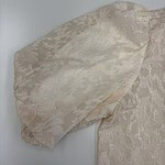 Close-up of a cream lace dress sleeve showcasing intricate floral patterns and delicate fabric texture.