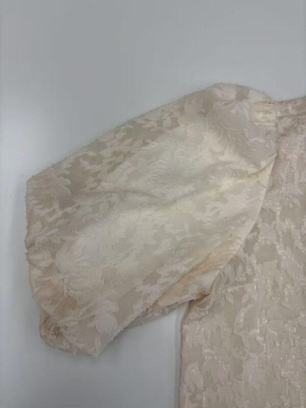 Close-up of a cream lace dress sleeve showcasing intricate floral patterns and delicate fabric texture.