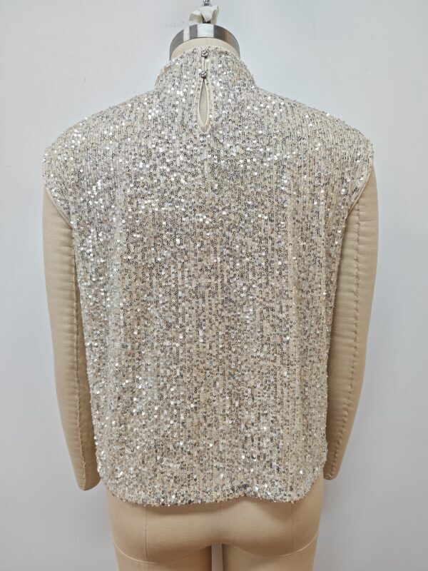 Close-up of a women's jacket with intricate sequin embellishments and beige sleeves, showcasing luxury fashion details.