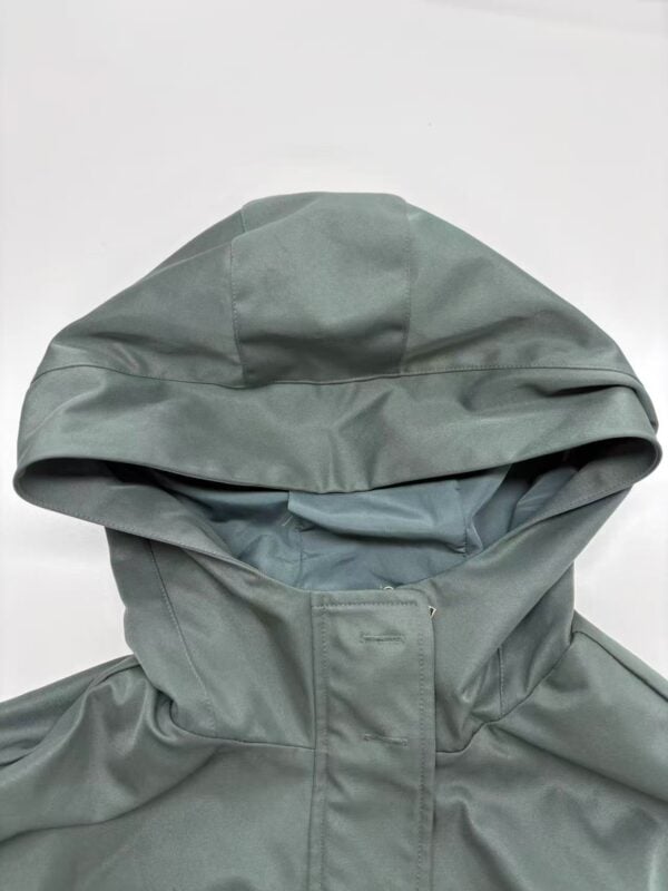 Close-up of a modern green hooded jacket with a high collar, made from waterproof material, perfect for outdoor fashion and weather protection.