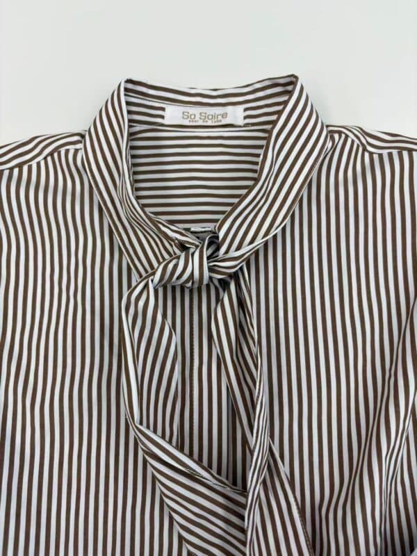 Close-up of a stylish striped blouse with a tie at the collar, perfect for fashion-forward women. Features brown and white vertical stripes and a comfortable fit.