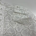 Close-up of white fabric with intricate heart-shaped embroidery and eyelet details, perfect for fashion or craft projects.