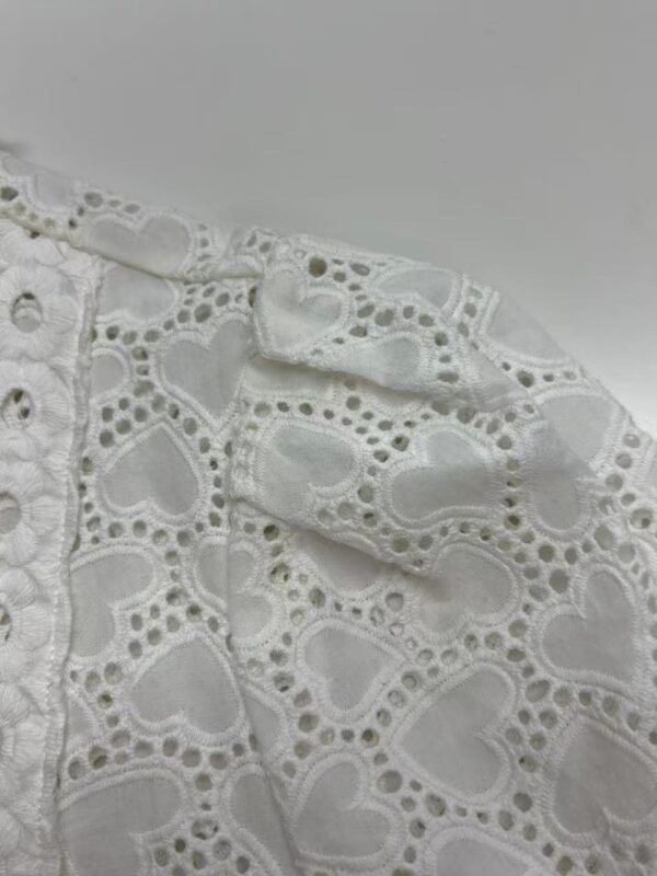 Close-up of white fabric with intricate heart-shaped embroidery and eyelet details, perfect for fashion or craft projects.