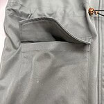 Close-up of gray workwear pants featuring a large front pocket and durable fabric, ideal for professional or casual wear.