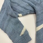 Close-up of a blue knitted sweater with cream-colored stripes, showcasing detailed knitting pattern and texture.