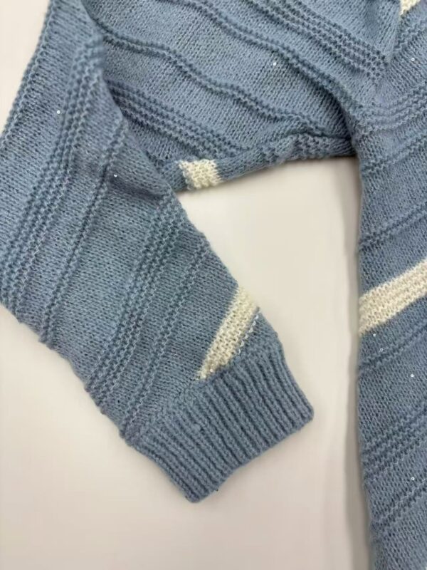 Close-up of a blue knitted sweater with cream-colored stripes, showcasing detailed knitting pattern and texture.